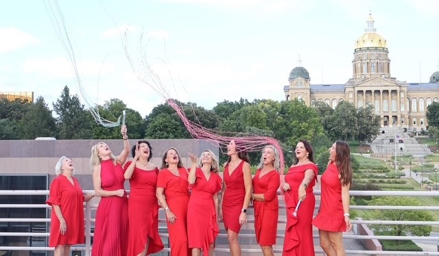 Group of women in red dresses waving red streamers in front of the Iowa Capitol Building.